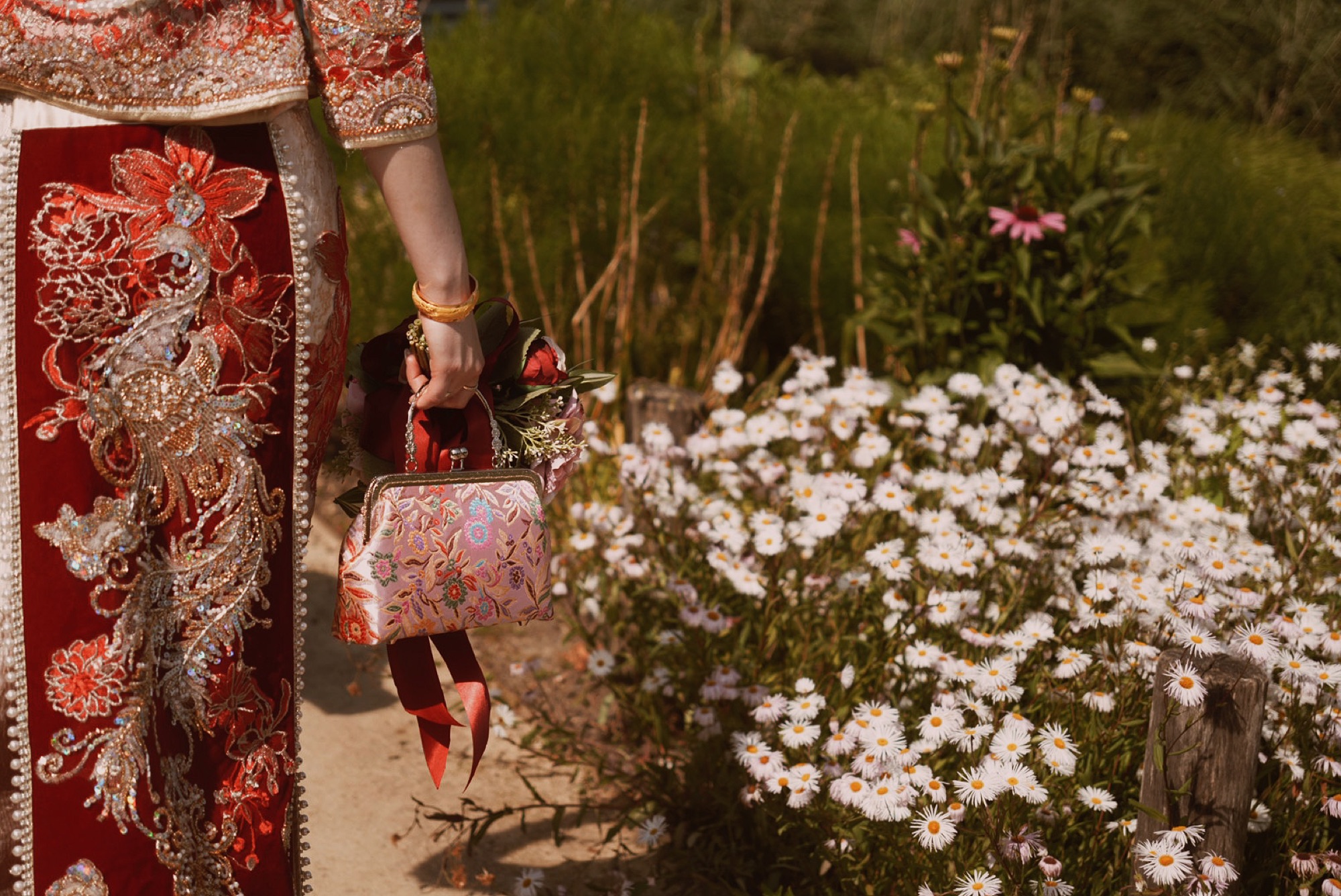 Bruid in traditionele rode geborduurde trouwjurk met bloemenboeket tussen wilde bloemen